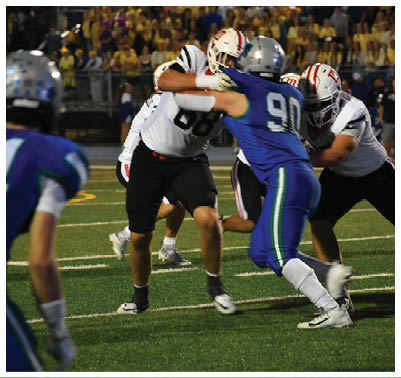 Two football players in blue and white uniforms are engaged in a blocking action on a field with a crowd in the background. Description generated by AI