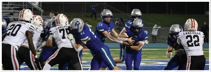 People in blue and white football uniforms are engaged in a play on a football field with a blue and white logo in the background. Description generated by AI