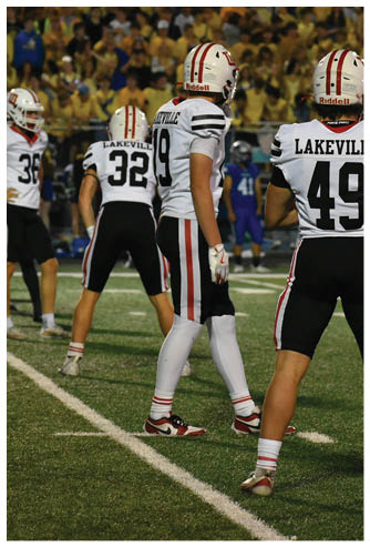 Several people wearing white football uniforms with “Lakeville" on the back are standing on a football field during a game. Description generated by AI