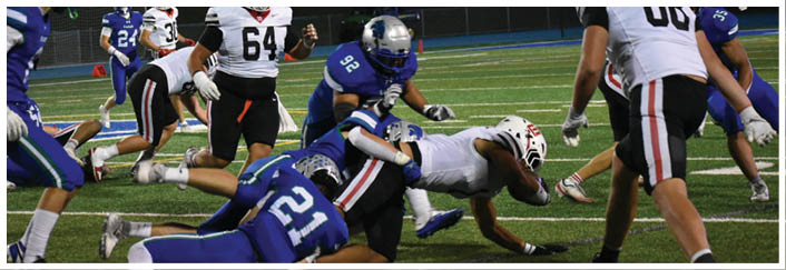 People in football uniforms are actively engaged in a tackle on a green field during a game. Description generated by AI