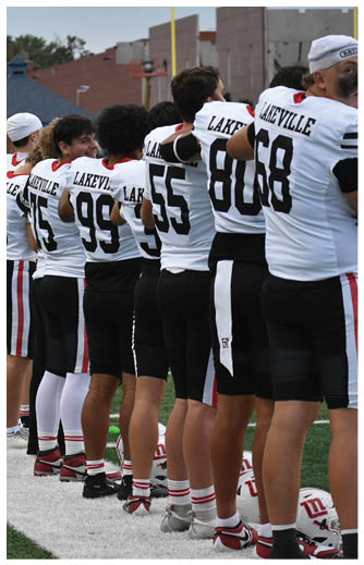 A line of people wearing matching sports uniforms stands on the edge of a football field with a football resting on the turf nearby. Description generated by AI