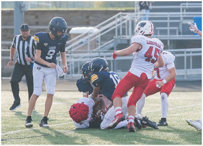 Several people in football uniforms are engaged in a play on a grassy field with one person on the ground holding the ball while others surround them. Description generated by AI