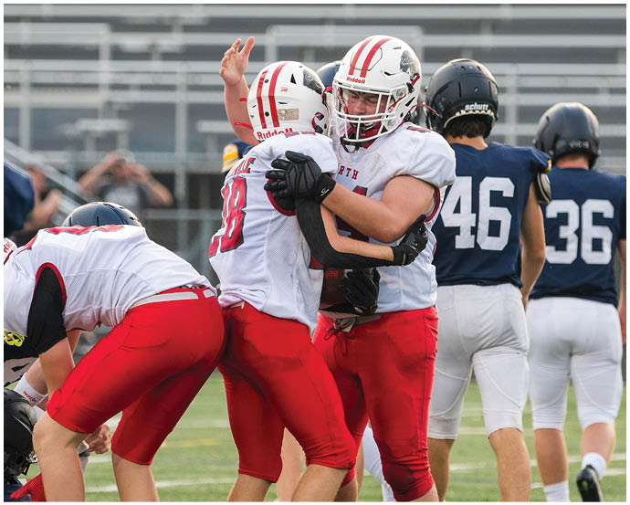 Players in red and white football uniforms celebrate on a field while players in blue and white uniforms walk away in the background. Description generated by AI
