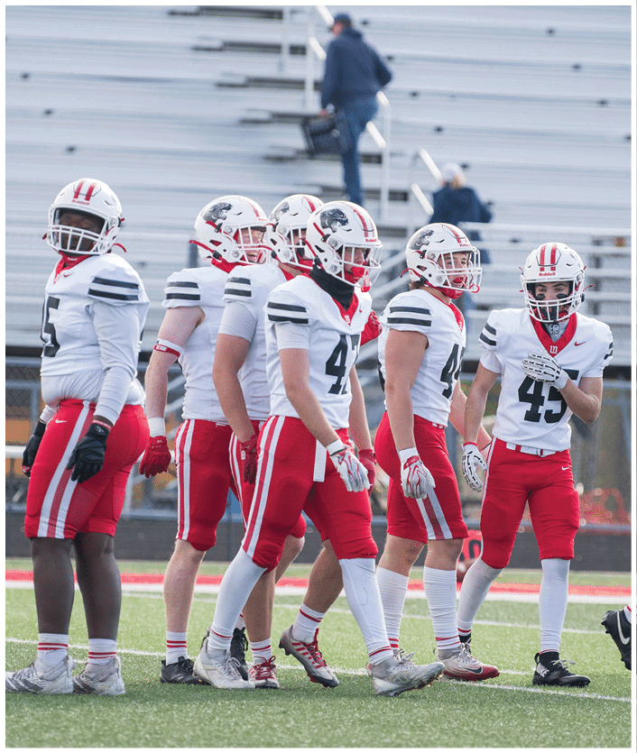 A group of people wearing white and red football uniforms are standing on a field with empty bleachers in the background. Description generated by AI