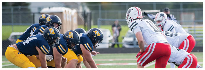 Two opposing American football teams are lined up facing each other on a field, preparing for a play during a game. Description generated by AI