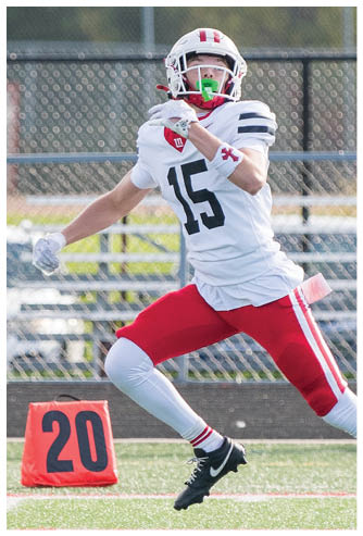 A person wearing a white football uniform with the number 15 is running on a field near an orange marker displaying the number 20. Description generated by AI