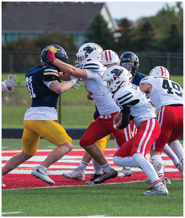 Three people in football uniforms are actively playing on a field with one person preparing to catch or throw a ball. Description generated by AI