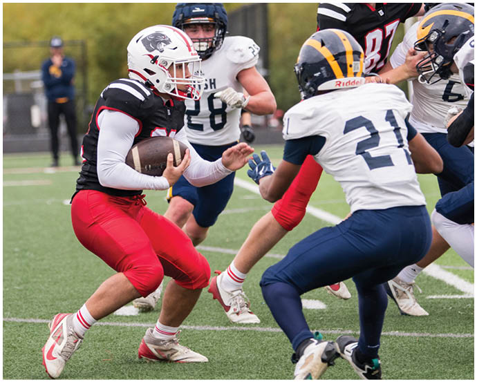 A person in a black and red football uniform is holding a football and running while being pursued by two people in white and blue football uniforms on a grassy field. Description generated by AI