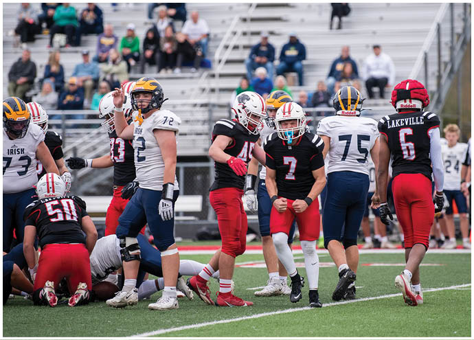 People wearing football uniforms are on a field with one person in a white jersey raising an arm while others in black and red uniforms stand or kneel nearby. Description generated by AI