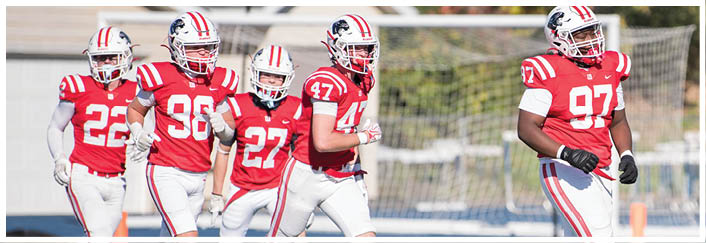 People wearing red and white football uniforms are walking on a grassy field near a goalpost. Description generated by AI