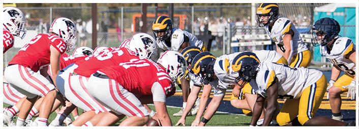 A group of people in red and white sports uniforms are lined up on a football field facing a group of people in black and yellow uniforms, preparing for a play. Description generated by AI