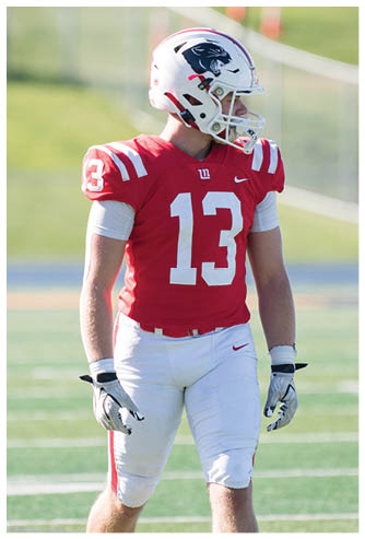 A person wearing a red football jersey with the number 13 and a white helmet stands on a football field. Description generated by AI