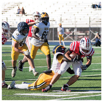 A person in a red and white striped football uniform is running with the ball while being tackled by a person in a white and yellow uniform on a football field. Description generated by AI