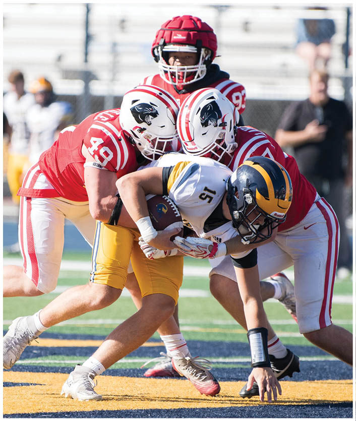 Three people in football uniforms are tackling a player in a white and yellow uniform who is holding a football on a field. Description generated by AI
