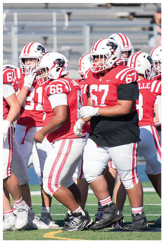 Several people wearing red and white football uniforms and helmets are standing together on a field. Description generated by AI