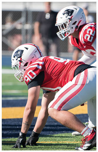 Two people in red and white football uniforms and helmets are positioned on a field, preparing for a play. Description generated by AI