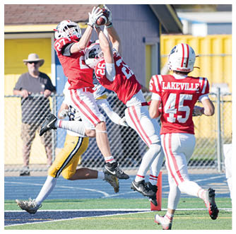 A person in a red sports uniform is jumping to catch a ball while another person in a yellow sports uniform attempts to block them on a football field with spectators and a photographer in the background. Description generated by AI