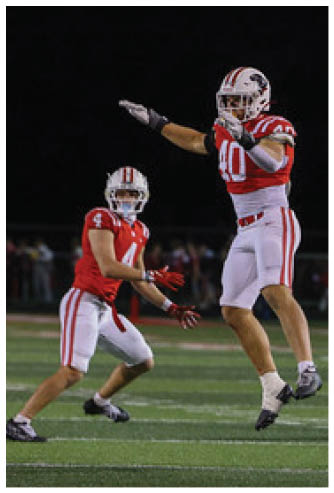 A person wearing a red and white football uniform with the number 40 is standing on a field, pointing forward. Description generated by AI