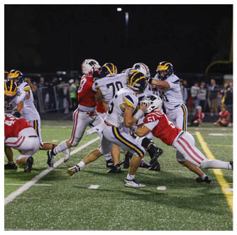 People wearing football uniforms are actively engaged in a play on a grassy field during a game. Description generated by AI