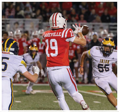 Two people in football uniforms are engaged in a play on a field with one person catching a football while the other approaches. Description generated by AI