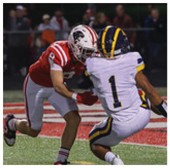 Two football players in action on a field, one wearing a red and white uniform and the other in a white uniform with blue and yellow accents, with the player in white crouching and the player in red reaching toward them. Description generated by AI