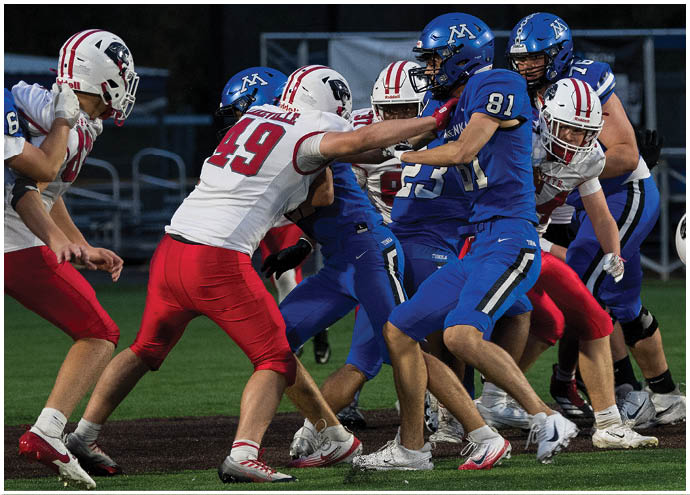 People wearing red and blue football uniforms are engaged in a play on a football field during a game. Description generated by AI