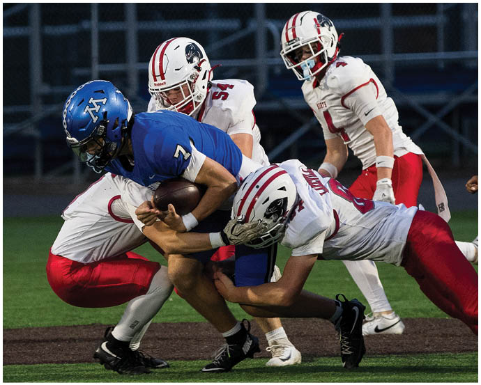A group of people in football uniforms are engaged in a tackle on a field during a game. Description generated by AI