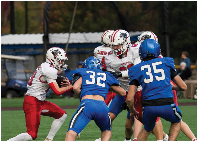 Several people wearing blue and white football uniforms are engaged in a play on a green field with trees in the background. Description generated by AI