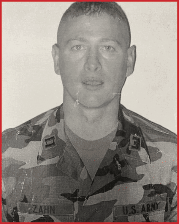 Person wearing a U.S. Army camouflage uniform with the name tag “ZAHN" looking directly at the camera against a plain background. Description generated by AI