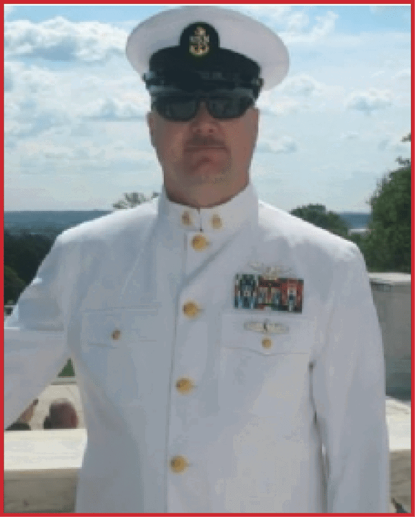 A person wearing a white military dress uniform with medals and a white peaked cap stands outdoors against a partly cloudy sky. Description generated by AI