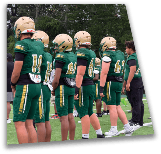 A group of people wearing green football uniforms stand in a line on a grassy field. Description generated by AI