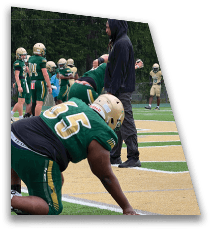 A person wearing a green football uniform with the number 75 is kneeling on one knee on a football field near the sideline. Description generated by AI