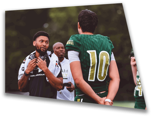 People on a football field include a player in a green uniform holding a helmet and two others standing nearby, one with a towel around the neck. Description generated by AI