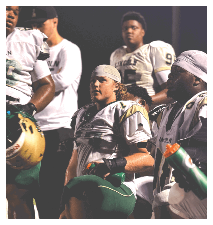 A football game is in progress with players on the field. One player is throwing a football while another player is trying to catch it. The players are wearing uniforms and are actively engaged in the game. AI generated content