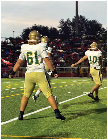 Three people wearing football uniforms with gold helmets and white and yellow jerseys are on a football field with a crowd in the background. Description generated by AI