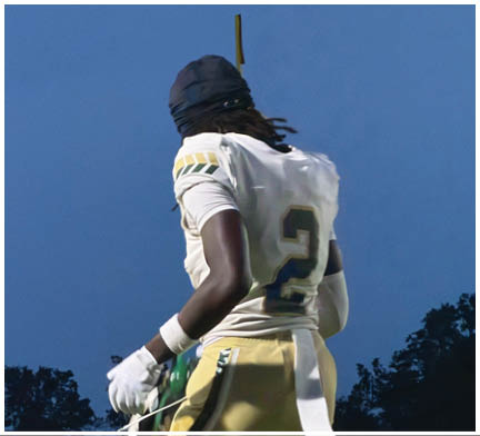 A person wearing a dark head covering and a white garment with green and yellow patterns is seen from behind against a clear blue sky. Description generated by AI