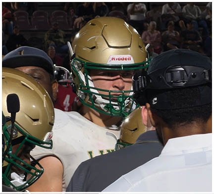 Three people are standing close together, one wearing a white shirt and black cap, another in a gray shirt, and the third in a white sports uniform with a green helmet. Description generated by AI