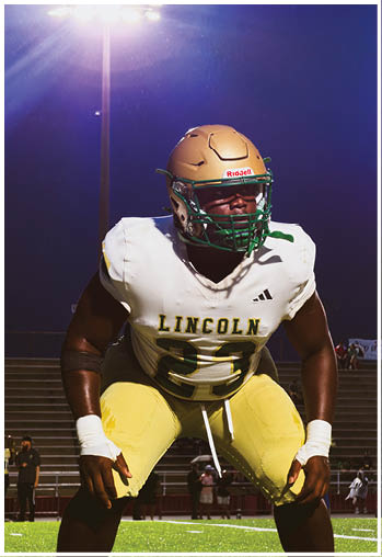 Person wearing a gold football helmet with a green faceguard and a white jersey against a dark blue background. Description generated by AI