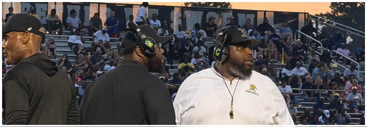 Four football players wearing gold helmets and white uniforms are positioned in front of a scoreboard at Crestview High School during a game. Description generated by AI