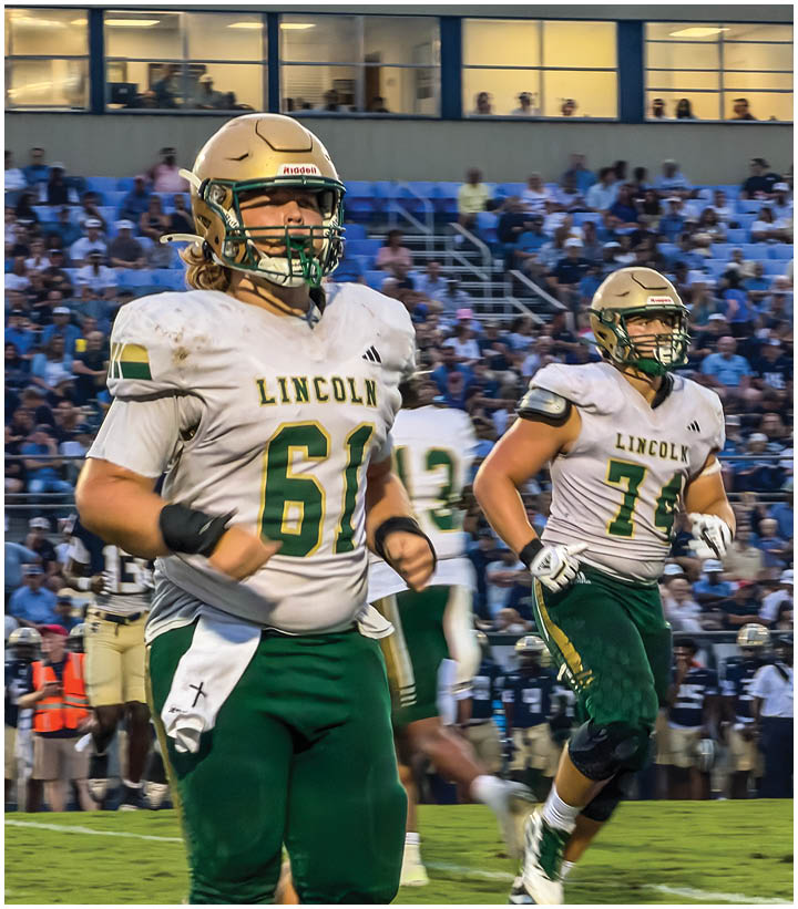 Several people wearing gold helmets and white and gold football uniforms are running on a football field during a game. Description generated by AI