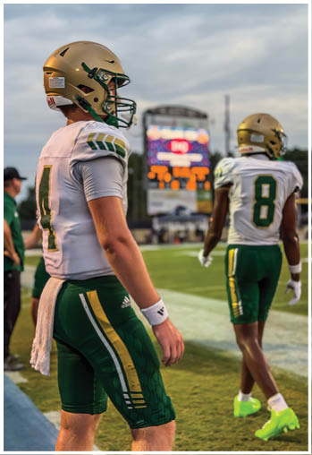 A person wearing a football uniform with the number 6 and the word Lincoln on the jersey stands on a field under bright stadium lights at night. Description generated by AI