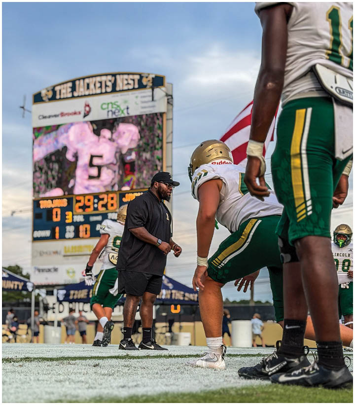 Three people in football uniforms and helmets are closely positioned, appearing focused and attentive during a game or practice. Description generated by AI