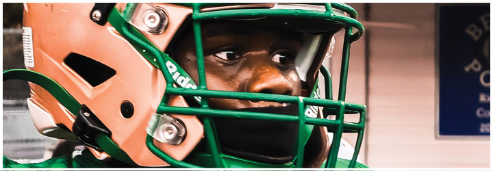 A close-up of a worn beige football helmet with a green faceguard and the brand name Riddell on the front. Description generated by AI
