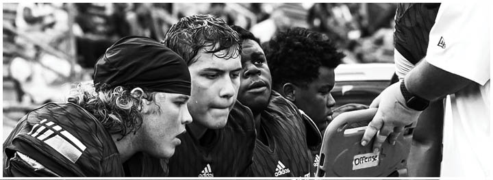 A person wearing a head covering and sportswear is looking down while several people sit in blurred stadium bleachers in the background. Description generated by AI