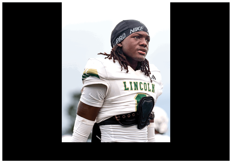 A person wearing a white football jersey with “LINCOLN" written on it and a black Nike headband is looking to the side. Description generated by AI