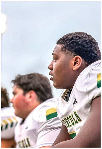 Two people wearing white sports jerseys with green and yellow accents are sitting closely together, appearing focused and engaged. Description generated by AI