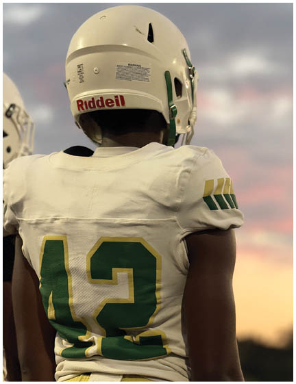 A person wearing a white football jersey with the number 42 and a white helmet stands outdoors during sunset. Description generated by AI