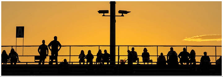 A tall light pole with multiple bright floodlights is set against a cloudy sky at dusk. Description generated by AI
