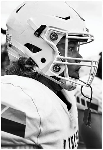 A person wearing a football helmet and jersey is looking to the side, appearing focused and ready for a game. Description generated by AI