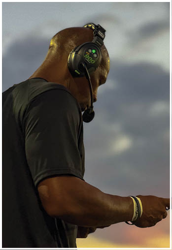 A person wearing a headset with a microphone and a dark shirt is looking down while standing outdoors against a cloudy sky. Description generated by AI